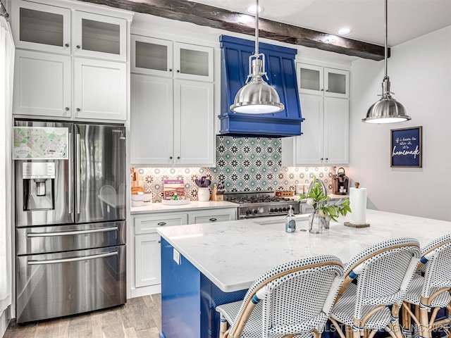 kitchen featuring light wood finished floors, backsplash, a breakfast bar, beam ceiling, and stainless steel appliances