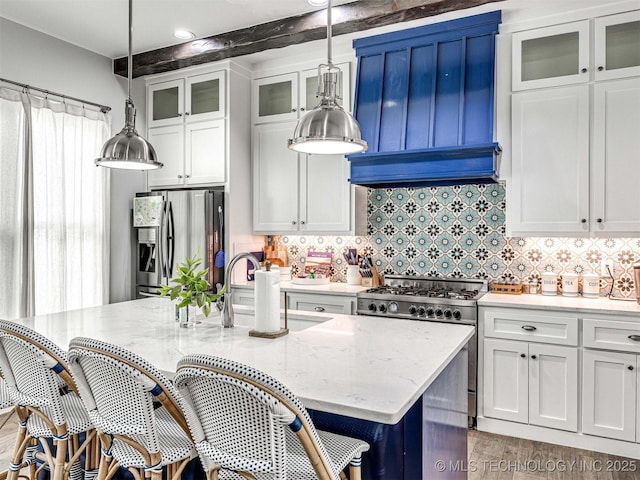 kitchen featuring a breakfast bar, light stone counters, decorative backsplash, appliances with stainless steel finishes, and white cabinets