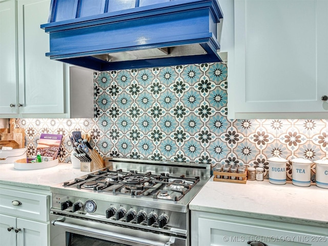 kitchen featuring tasteful backsplash, light stone countertops, custom range hood, high end stainless steel range oven, and white cabinetry