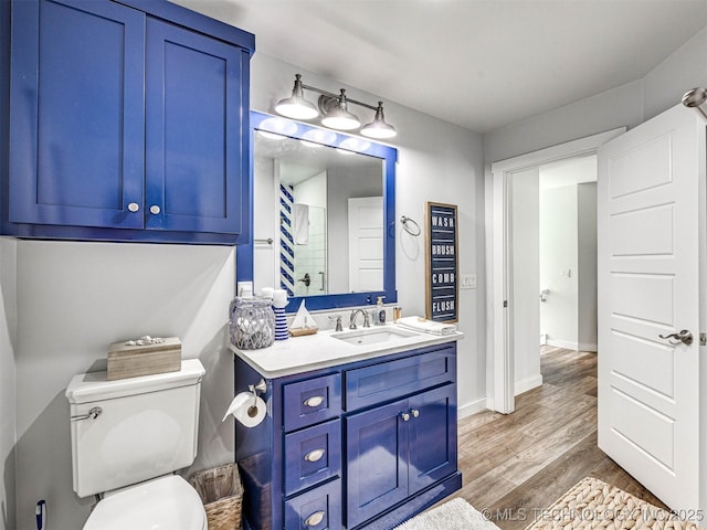 bathroom featuring baseboards, toilet, wood finished floors, and vanity