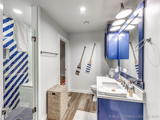 bathroom featuring visible vents, toilet, wood finished floors, a shower stall, and vanity