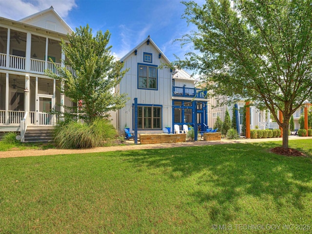 rear view of property with a yard, a balcony, board and batten siding, and a ceiling fan