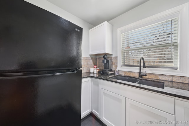 kitchen featuring dark stone counters, freestanding refrigerator, a sink, decorative backsplash, and white cabinetry