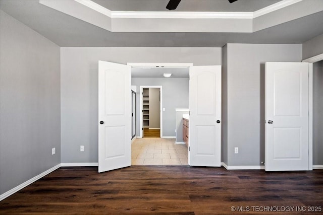 unfurnished bedroom featuring a tray ceiling, baseboards, and wood finished floors