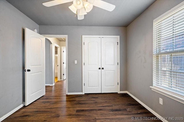 unfurnished bedroom featuring multiple windows, arched walkways, a closet, and dark wood finished floors