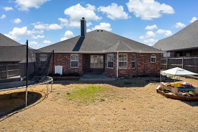 rear view of house featuring fence, a trampoline, a patio area, and brick siding