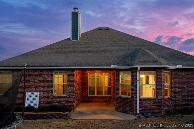 rear view of property with a patio area, brick siding, roof with shingles, and a chimney