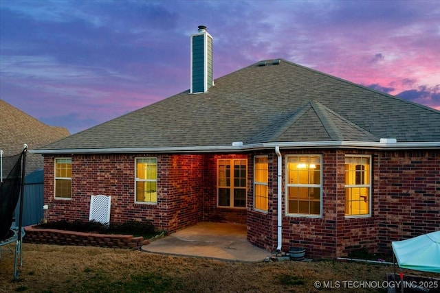 back of property featuring a trampoline, a chimney, brick siding, and a patio area