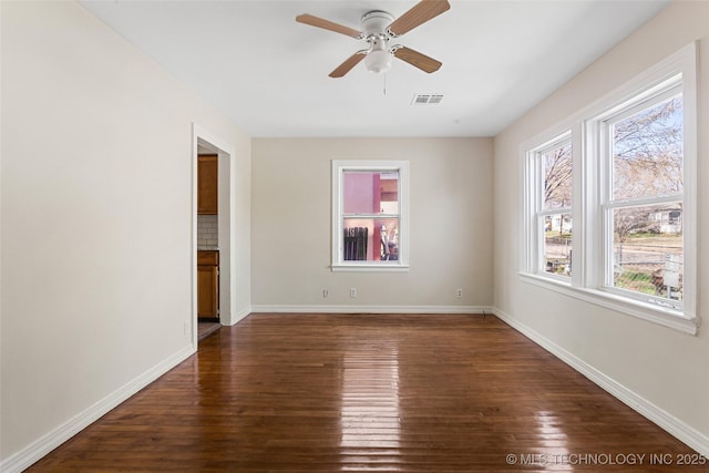 empty room with dark wood-style floors, visible vents, ceiling fan, and baseboards