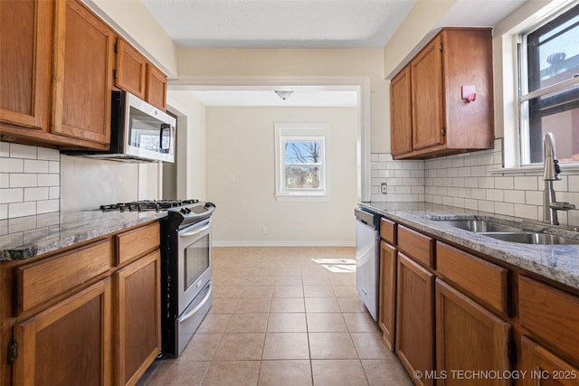 kitchen featuring brown cabinetry, baseboards, light tile patterned flooring, stainless steel appliances, and a sink