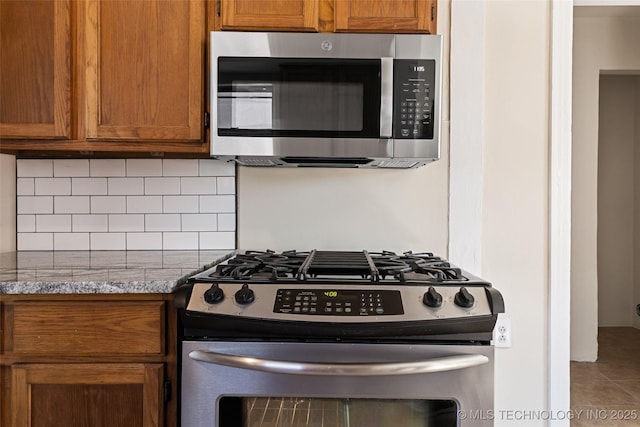 kitchen featuring light stone counters, stainless steel appliances, decorative backsplash, and brown cabinetry