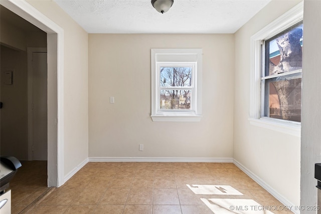 unfurnished room with baseboards, plenty of natural light, a textured ceiling, and light tile patterned flooring