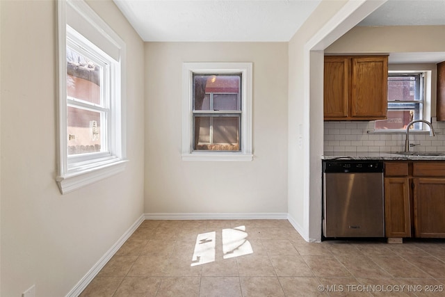 kitchen featuring brown cabinets, a sink, stainless steel dishwasher, decorative backsplash, and baseboards