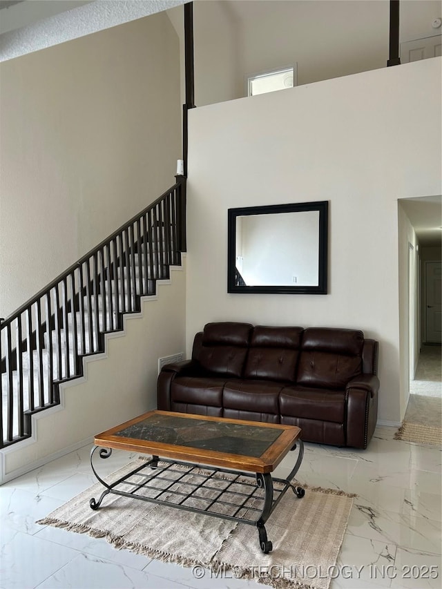 living area featuring stairway, marble finish floor, baseboards, and a towering ceiling