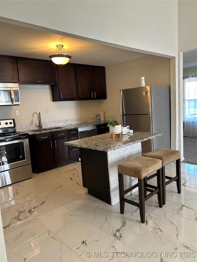 kitchen with marble finish floor, a sink, a kitchen breakfast bar, appliances with stainless steel finishes, and light stone countertops