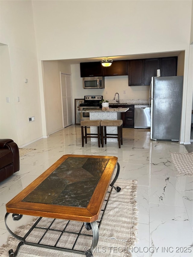 kitchen with a sink, a high ceiling, marble finish floor, and stainless steel appliances