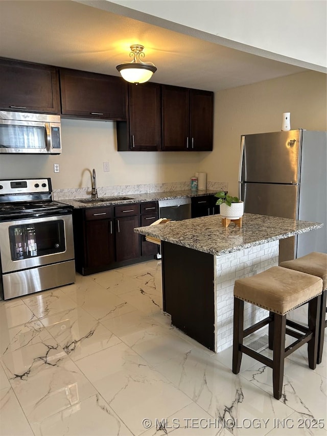 kitchen with light stone counters, a breakfast bar, a sink, appliances with stainless steel finishes, and marble finish floor