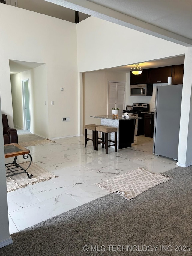 kitchen with a kitchen island, baseboards, a breakfast bar area, marble finish floor, and stainless steel appliances