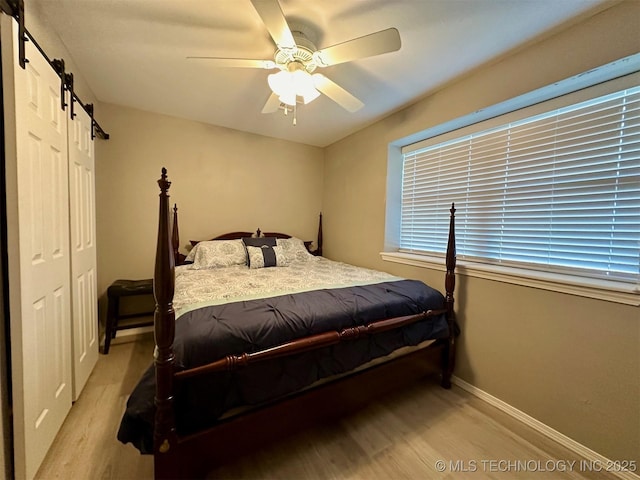 bedroom featuring light wood finished floors, ceiling fan, baseboards, and a barn door