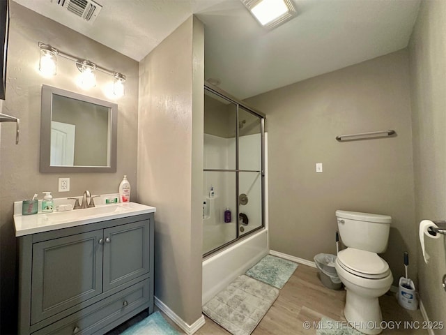 bathroom with visible vents, toilet, wood finished floors, combined bath / shower with glass door, and vanity