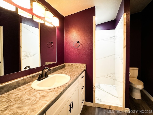 full bath featuring toilet, vanity, baseboards, and a textured wall