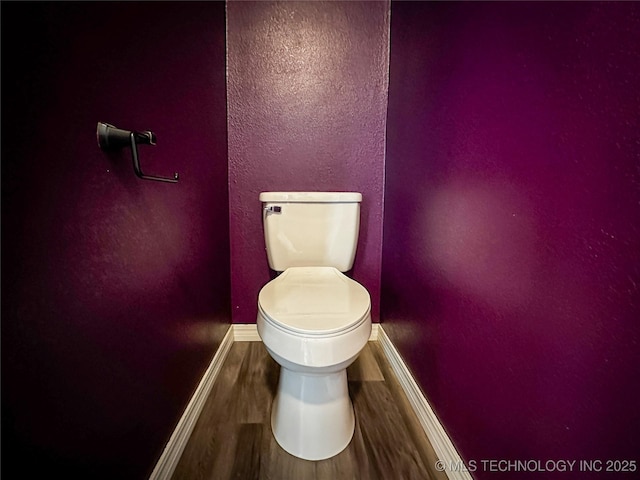 bathroom with baseboards, toilet, wood finished floors, and a textured wall