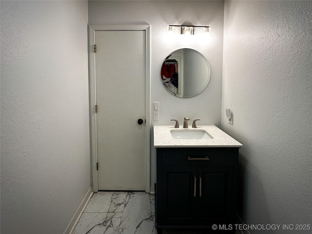 bathroom with vanity, baseboards, marble finish floor, and a textured wall