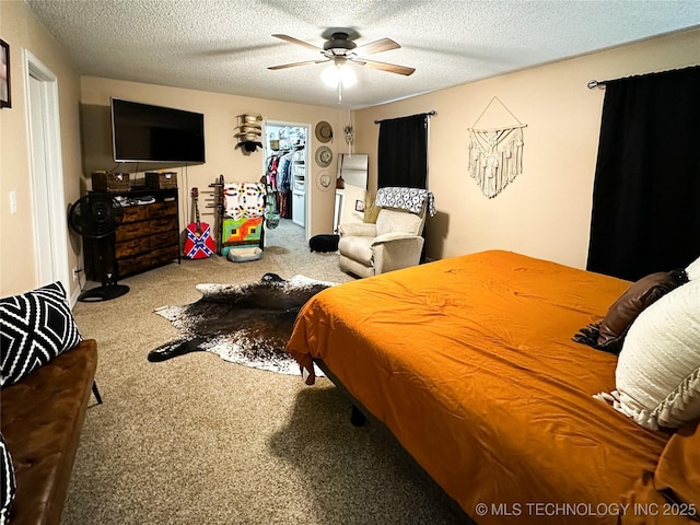 carpeted bedroom with a textured ceiling, a walk in closet, and a ceiling fan