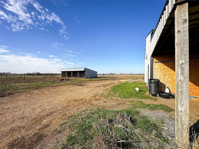 view of yard with a rural view, dirt driveway, fence, an outdoor structure, and a pole building