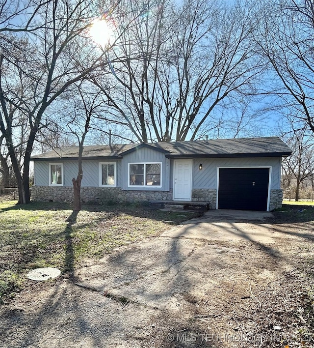 ranch-style home with a garage, stone siding, and driveway