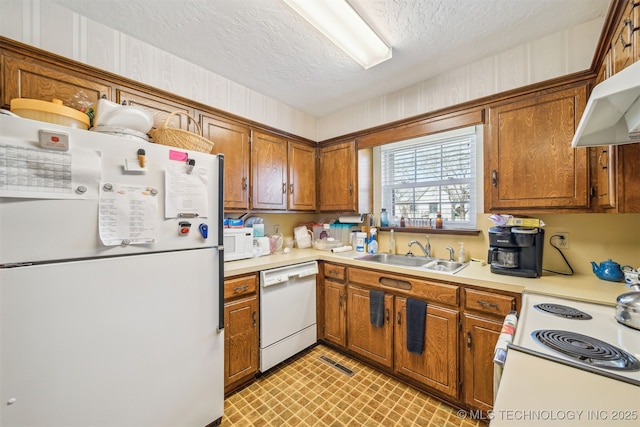 kitchen with a sink, white appliances, brown cabinetry, and light countertops