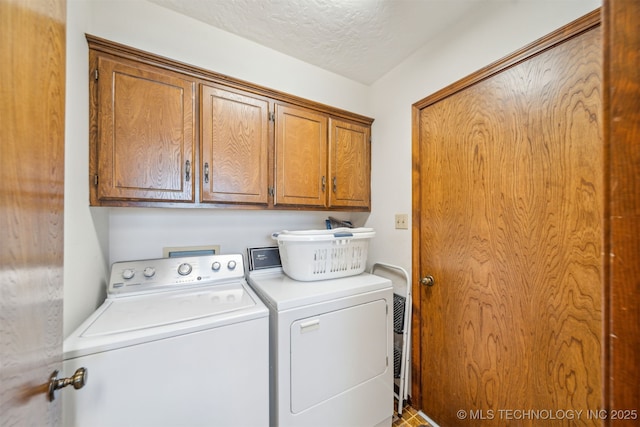 washroom featuring washing machine and clothes dryer, cabinet space, and a textured ceiling