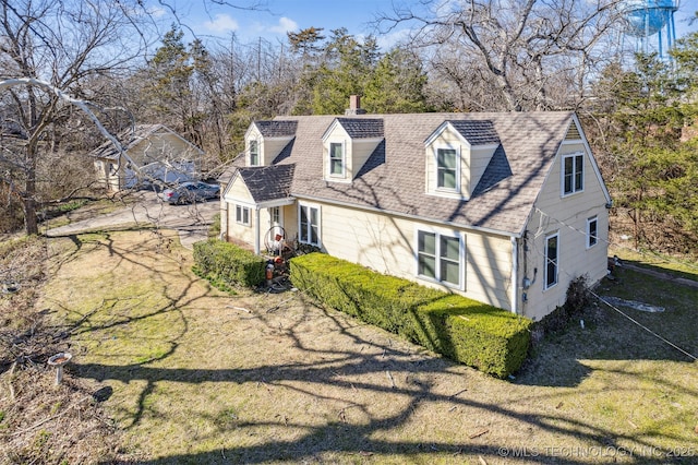 exterior space featuring a front lawn, a chimney, and a shingled roof