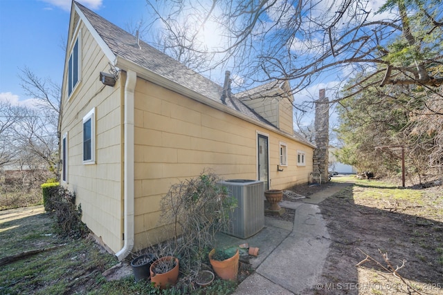 view of property exterior with roof with shingles, central AC unit, and a chimney