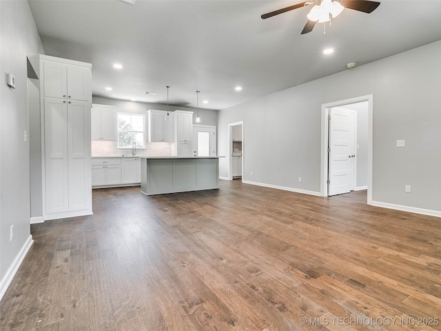 unfurnished living room featuring a ceiling fan, wood finished floors, baseboards, recessed lighting, and a sink