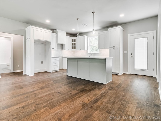 kitchen with a kitchen island, a sink, dark wood-type flooring, white cabinets, and backsplash