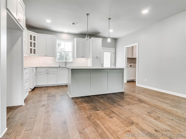 kitchen featuring light wood finished floors, visible vents, backsplash, a center island, and white cabinetry