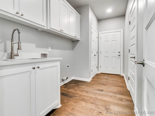 laundry room featuring baseboards, light wood-style floors, cabinet space, electric dryer hookup, and a sink