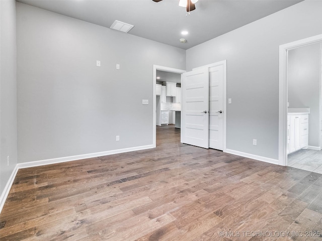 unfurnished bedroom with visible vents, baseboards, wood finished floors, ensuite bath, and a ceiling fan