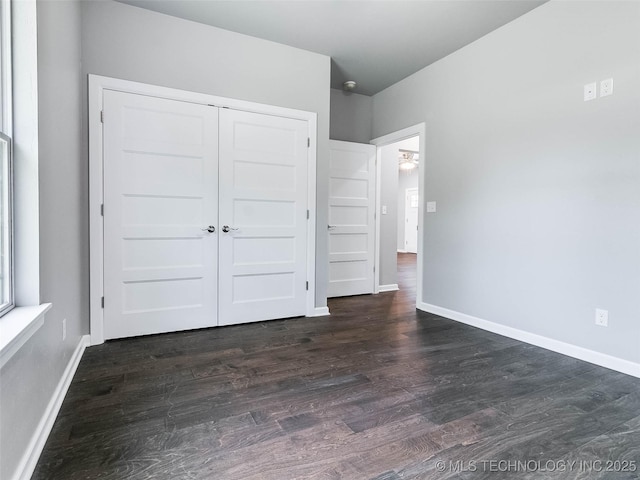 unfurnished bedroom featuring dark wood-style floors, a closet, and baseboards