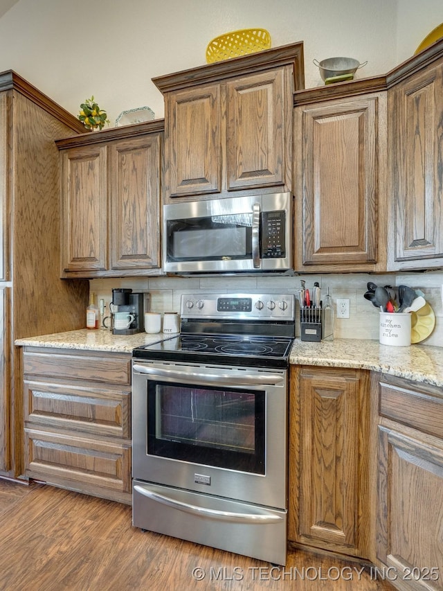 kitchen featuring light stone counters, decorative backsplash, brown cabinets, wood finished floors, and stainless steel appliances