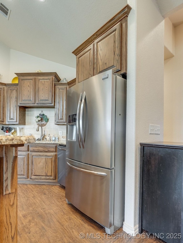 kitchen featuring visible vents, lofted ceiling, stainless steel appliances, light wood-style floors, and backsplash