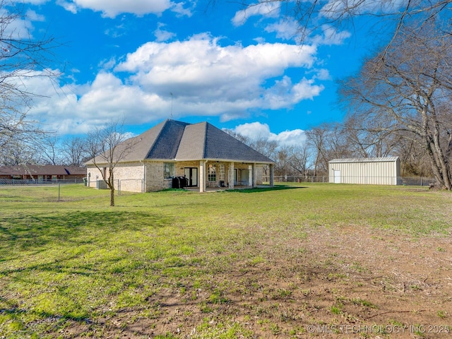 rear view of property with brick siding, roof with shingles, a yard, and fence