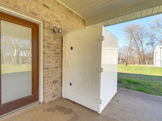 doorway to property featuring a yard, fence, and brick siding