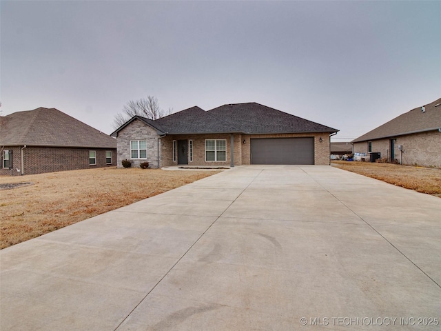 single story home with central AC unit, an attached garage, a shingled roof, concrete driveway, and brick siding