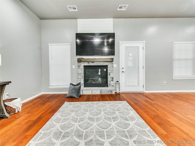 living room featuring wood finished floors, a fireplace, visible vents, and baseboards