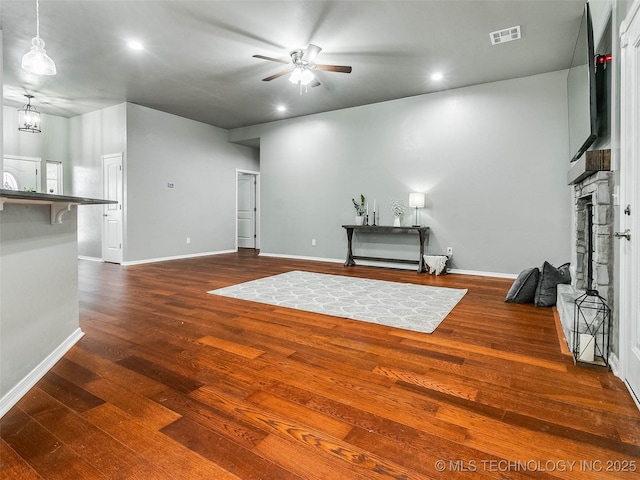 unfurnished living room featuring visible vents, a fireplace with raised hearth, dark wood finished floors, and ceiling fan with notable chandelier