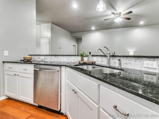 kitchen with a sink, stainless steel dishwasher, white cabinetry, dark stone counters, and light wood finished floors