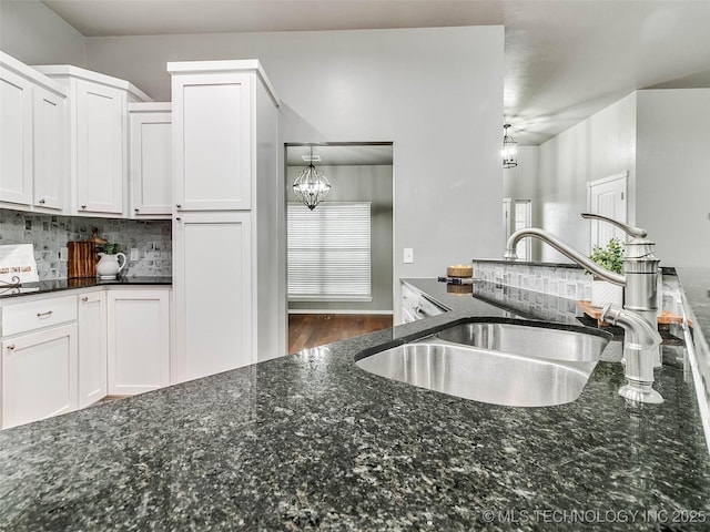 kitchen featuring tasteful backsplash, a chandelier, dark stone countertops, white cabinets, and a sink