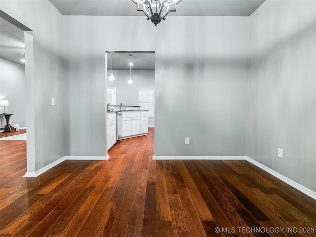 unfurnished dining area featuring a notable chandelier, baseboards, and dark wood-style flooring